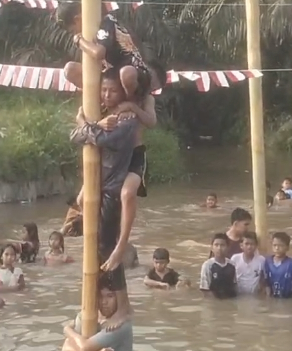 Peserta panjat pinang berjuang mencapai puncak di atas Sungai Tangguk Tinggal, Desa Air Terjun.